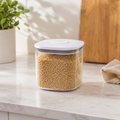 Clear 1L push top pantry container with a white lid filled with dry grains on a kitchen counter