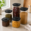 Five clear push top pantry containers with black lids displayed on a kitchen worktop